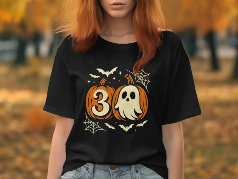 A woman with reddish hair wears a black t-shirt featuring a Halloween design of pumpkins, a ghost, and bats.