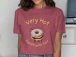 A woman wearing a maroon shirt with a donut graphic and text "Very Hot Handle with Care" in yellow.