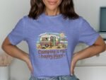 Woman wearing a blue t-shirt with a camping-themed design featuring a vintage camper, sun, and the text "Camping is my happy place."