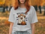A person wears a white t-shirt featuring a cartoon cow dressed as a ghost, with a jack-o'-lantern and bats.