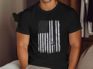 Man wearing a black t-shirt with a distressed American flag graphic, sitting on a bed.