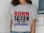 Woman wearing a gray t-shirt with the text "BORN FREE but LOVE EXPENSIVE," in red, black, and blue lettering.