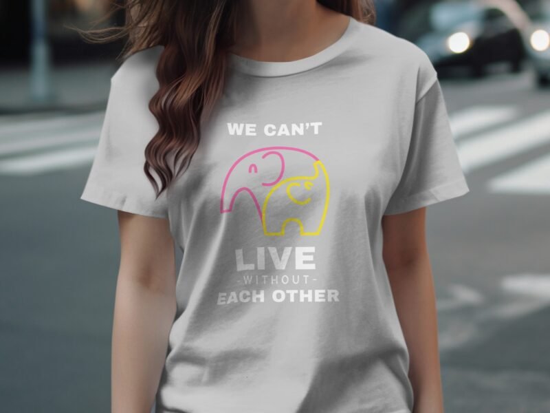 A woman wears a gray t-shirt with colorful elephant graphics and the text "WE CAN'T LIVE WITHOUT EACH OTHER."