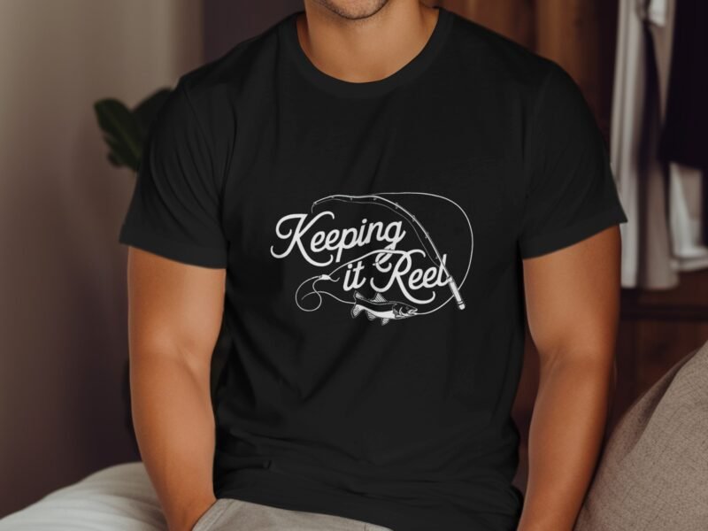 A man in a black t-shirt featuring the phrase "Keeping it Reel" with a fishing rod and fish graphic.