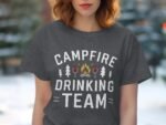 A woman wearing a dark gray t-shirt with "Campfire Drinking Team" graphic, surrounded by trees in a blurred background.