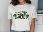 A woman wears a white t-shirt with the phrase "I'm not dirty, I'm Earthy" in green lettering, surrounded by leaf designs.