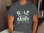 A man in a gray T-shirt with "GOLF DADDY MEMBERS ONLY" text and golf graphics. Background features wooden decor.