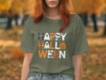 Person wearing a green "Happy Halloween" t-shirt with spooky graphics, surrounded by autumn foliage.