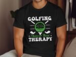 A person wearing a black t-shirt with the slogan "Golfing Cheaper Than Therapy" and a graphic of a golf ball.