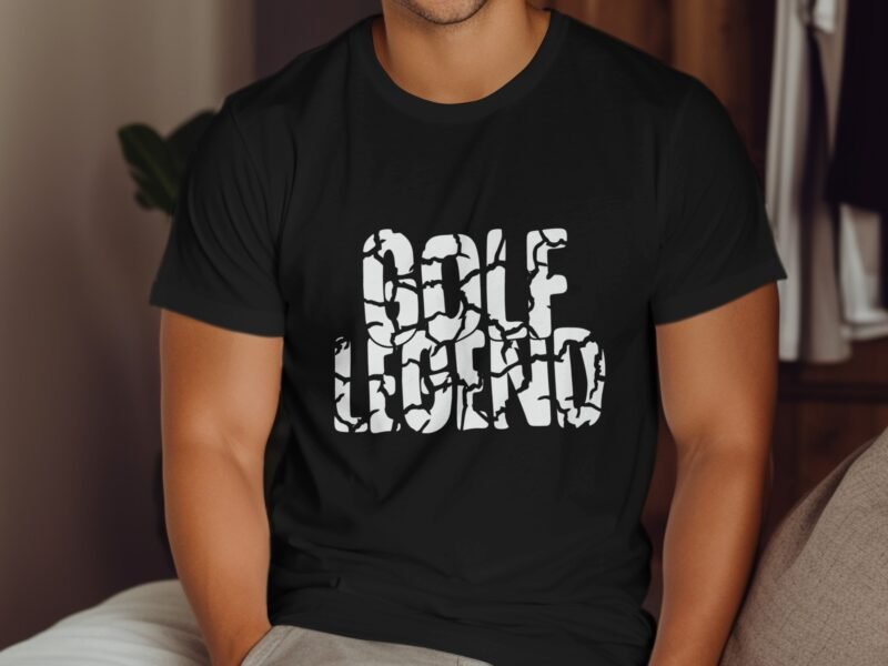 A man in a black t-shirt with the text "Golf Legend" in a cracked white font, sitting in a cozy interior space.