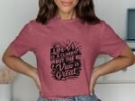 Person wearing a pink t-shirt with black inspirational text about life, mountains, and views in a bright room.