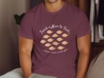A man wearing a maroon t-shirt with a fish graphic and the text "Teach a Man to Fish..." sits against a wall.