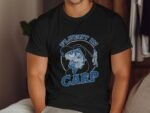 A man wearing a black t-shirt with a graphic of a fishing scene and the text "Fluent in Carp."