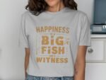 Woman in a gray t-shirt with "Happiness is a BIG FISH and a WITNESS" printed in orange lettering, smiling.