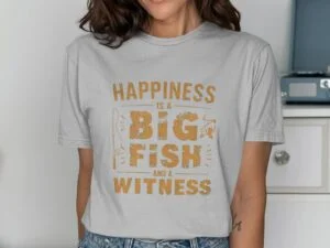 Woman in a gray t-shirt with "Happiness is a BIG FISH and a WITNESS" printed in orange lettering, smiling.