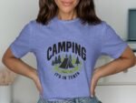 A woman wearing a purple t-shirt with "CAMPING IT'S IN TENTS" graphic, featuring a tent and trees design.