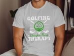 A man wears a light gray t-shirt with the text "GOLFING Cheaper Than THERAPY" and a green golfing graphic.