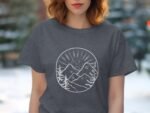 A woman with wavy hair wears a dark gray t-shirt featuring a mountain graphic with trees and sun rays.