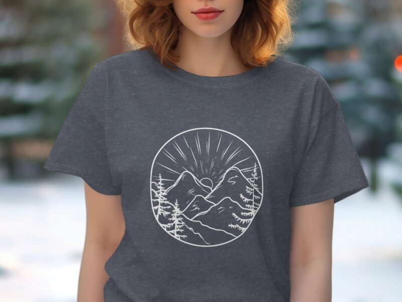 A woman with wavy hair wears a dark gray t-shirt featuring a mountain graphic with trees and sun rays.