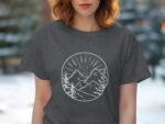 A woman with wavy hair wears a dark gray t-shirt featuring a white mountain landscape design.