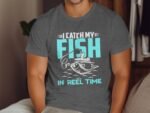 A man wearing a gray t-shirt with a fishing-themed graphic and text: "I CATCH MY FISH IN REEL TIME."