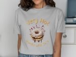 A woman wears a light gray t-shirt featuring a cartoon donut with icing and the text "Very Hot Handle With Care."