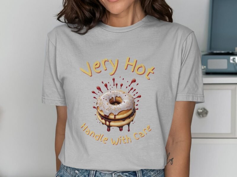 A woman wears a light gray t-shirt featuring a cartoon donut with icing and the text "Very Hot Handle With Care."