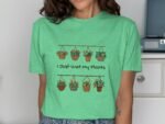 A woman wearing a green t-shirt with hanging flower pots and the phrase "I Just Wet My Plants" printed on it.