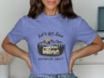 A woman in a blue t-shirt with a camper and mountains design, text reads "Let's Get Lost Adventure Awaits."