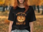 A woman in a black t-shirt with a pumpkin graphic and the text "If You've Got It, Haunt It" in an autumn setting.