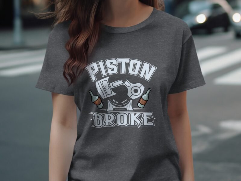 Woman wearing a gray t-shirt featuring the text "PISTON BROKE" with graphic elements, standing on a city street.