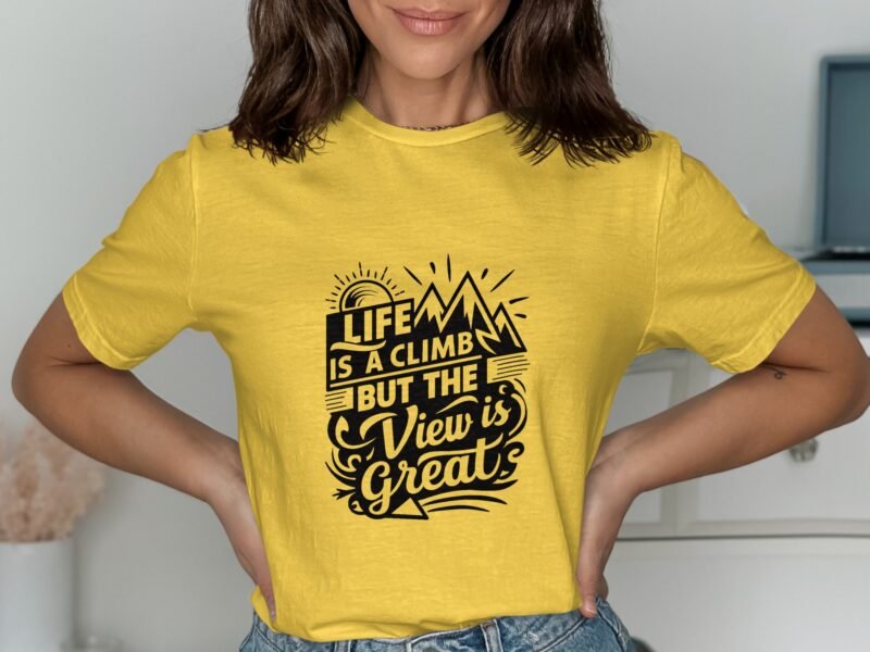 A woman in a yellow t-shirt displays a motivational graphic reading, "Life is a climb but the view is great."