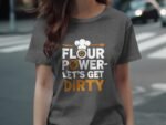 A woman in a gray t-shirt with the text "Flour Power - Let's Get Dirty" and a chef hat graphic stands outdoors.