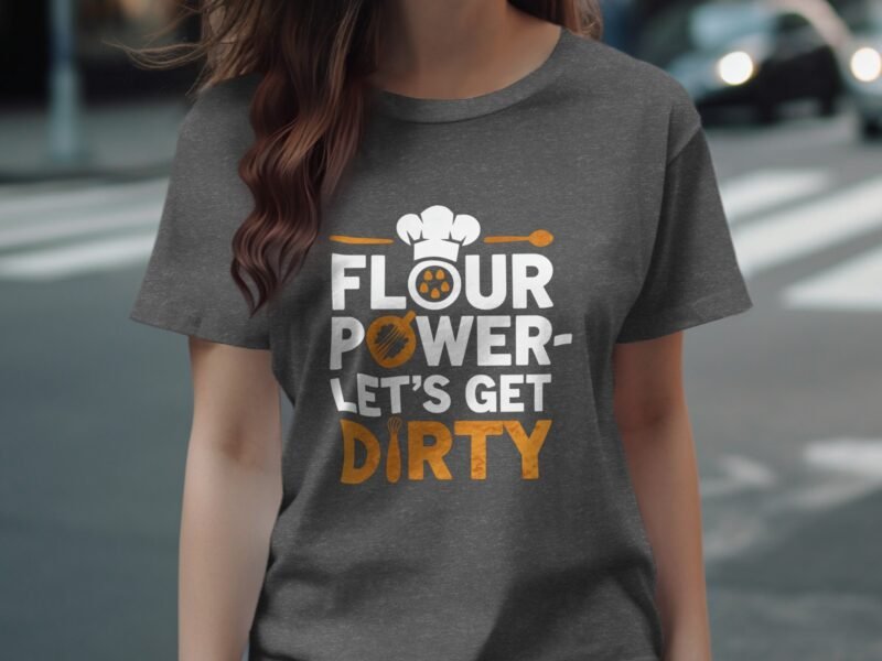 A woman in a gray t-shirt with the text "Flour Power - Let's Get Dirty" and a chef hat graphic stands outdoors.
