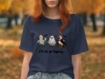 A woman in a navy t-shirt featuring cartoon chickens dressed as a mummy, ghost, and witch, with the text "Chick or Tweet."