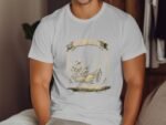 A man wearing a white t-shirt with a fishing graphic sits against a wooden backdrop, showcasing a casual look.