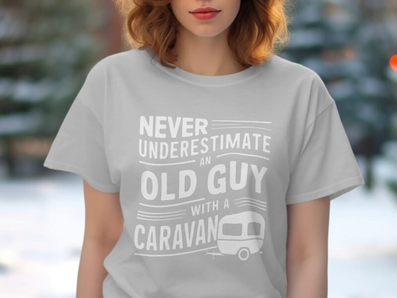 A woman wearing a gray t-shirt with text reading, "Never underestimate an old guy with a caravan." Background is blurred.