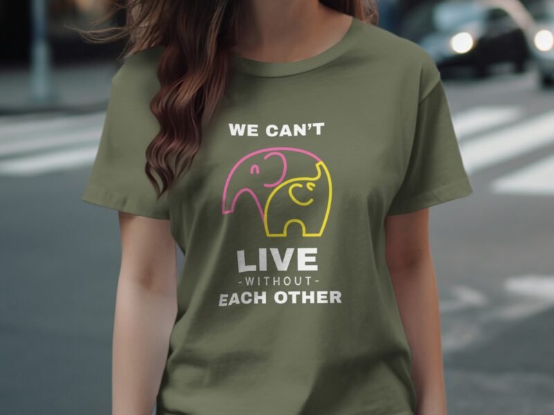 Woman wearing an olive green t-shirt featuring colorful elephants and the text “We can’t live without each other.”