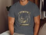 A man in a gray t-shirt featuring a fishing graphic and the text "GONE FISHIN'," sitting in a cozy indoor setting.