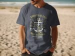A man wearing a navy blue t-shirt with an anchor graphic and the text "Born to Be Free" stands on a sandy beach.