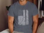 Man wearing a gray t-shirt with a vintage American flag design, seated on a couch in a cozy room.