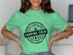 A woman wearing a green t-shirt with "Camping Crew" printed on it, showcasing a camping-themed design.