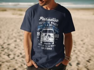 Man wearing a navy t-shirt with a beach-themed graphic featuring a retro van and palm trees, on a sandy beach.