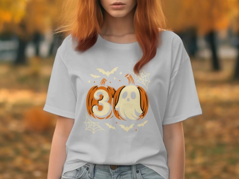 A woman with orange hair wears a gray t-shirt featuring Halloween-themed graphics of pumpkins, ghosts, and bats.
