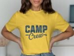 A person wearing a yellow t-shirt with "CAMP Crew" printed in blue, standing against a neutral background.