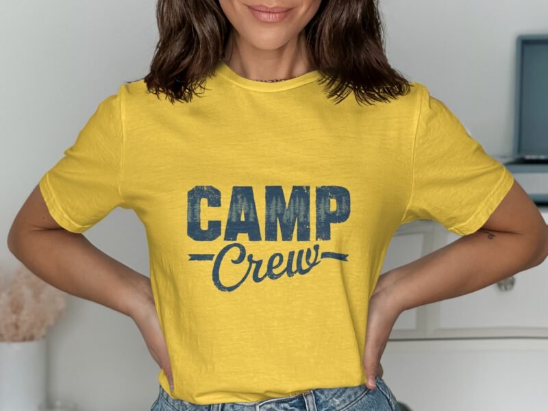 A person wearing a yellow t-shirt with "CAMP Crew" printed in blue, standing against a neutral background.