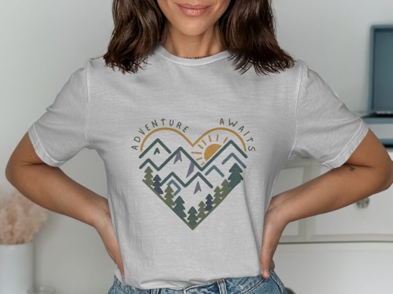 Woman wearing a white t-shirt with a heart design featuring mountains, trees, and the text "Adventure Awaits."