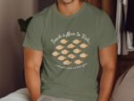Man wearing a green t-shirt with a fishing-themed quote and illustrations of fish. Cozy indoor setting.