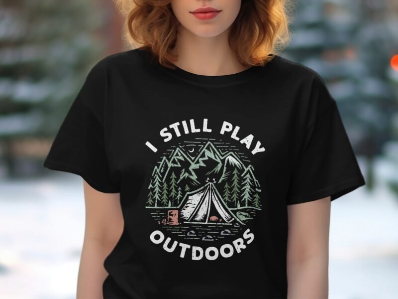 A woman wearing a black T-shirt featuring the text "I STILL PLAY OUTDOORS" with a camping design and trees.