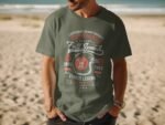 Man wearing a green t-shirt with racing graphic design, standing on a sandy beach, ocean in the background.
